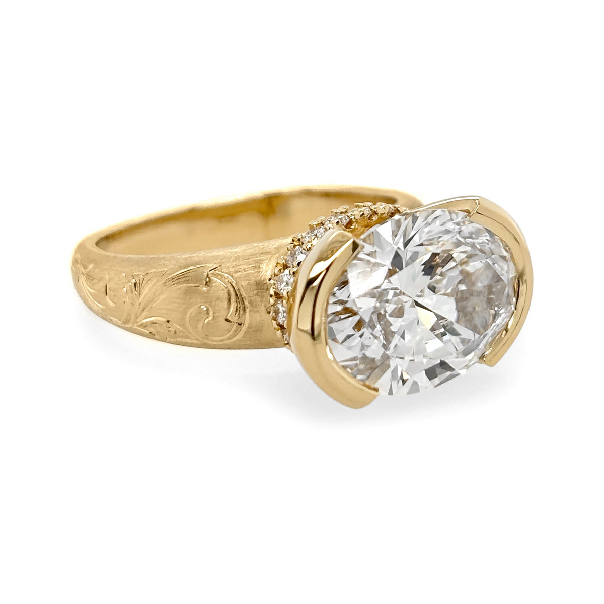 A yellow gold half bezel engagement ring featuring an east-west oval cut center stone and antique style engraving on the band.